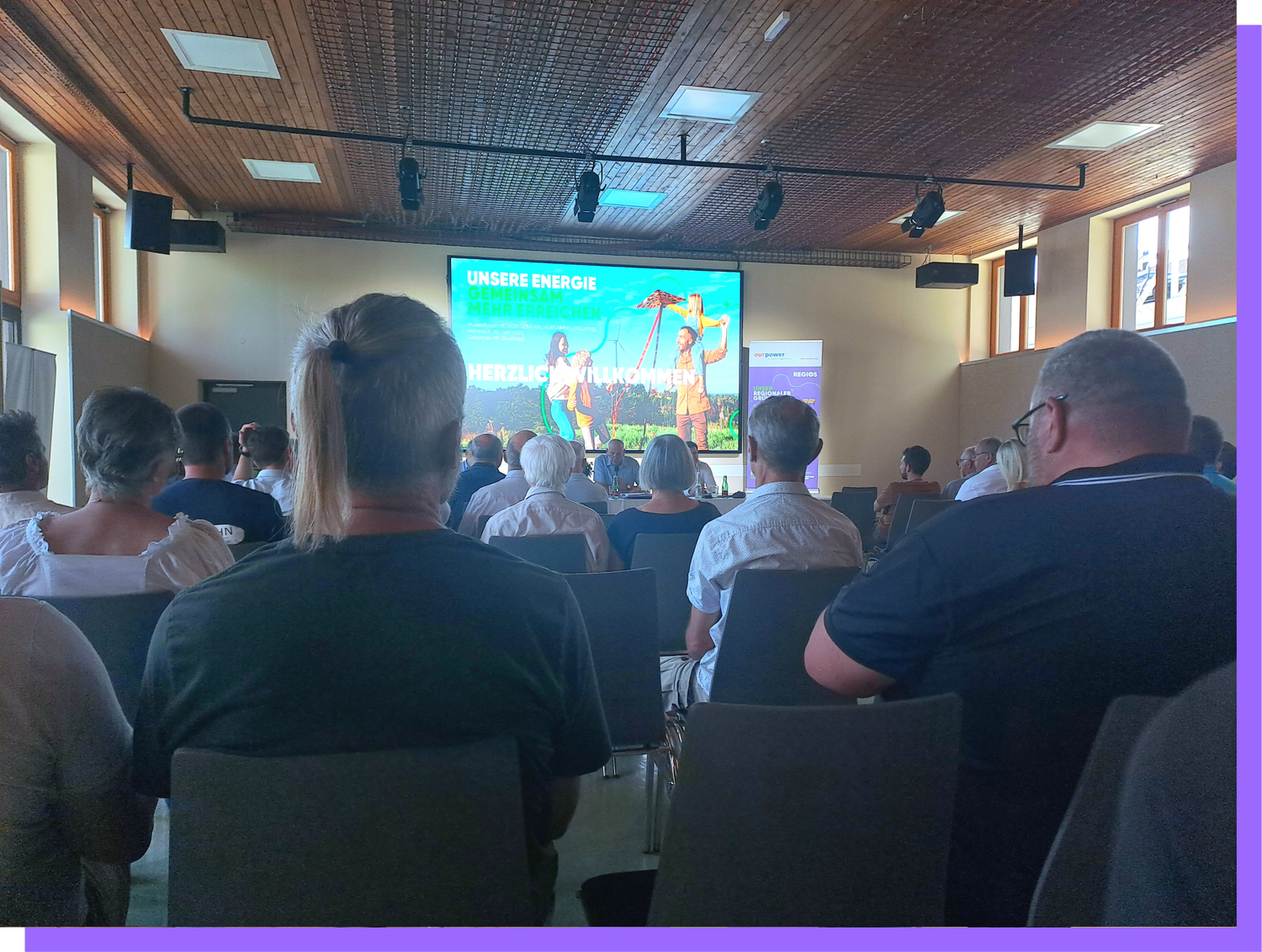 Konferenzraum mit Publikum, das auf eine Präsentationsleinwand blickt, auf der Energie und Nachhaltigkeit thematisiert werden, mit Sitzgelegenheiten und Vorträgern im Vordergrund.